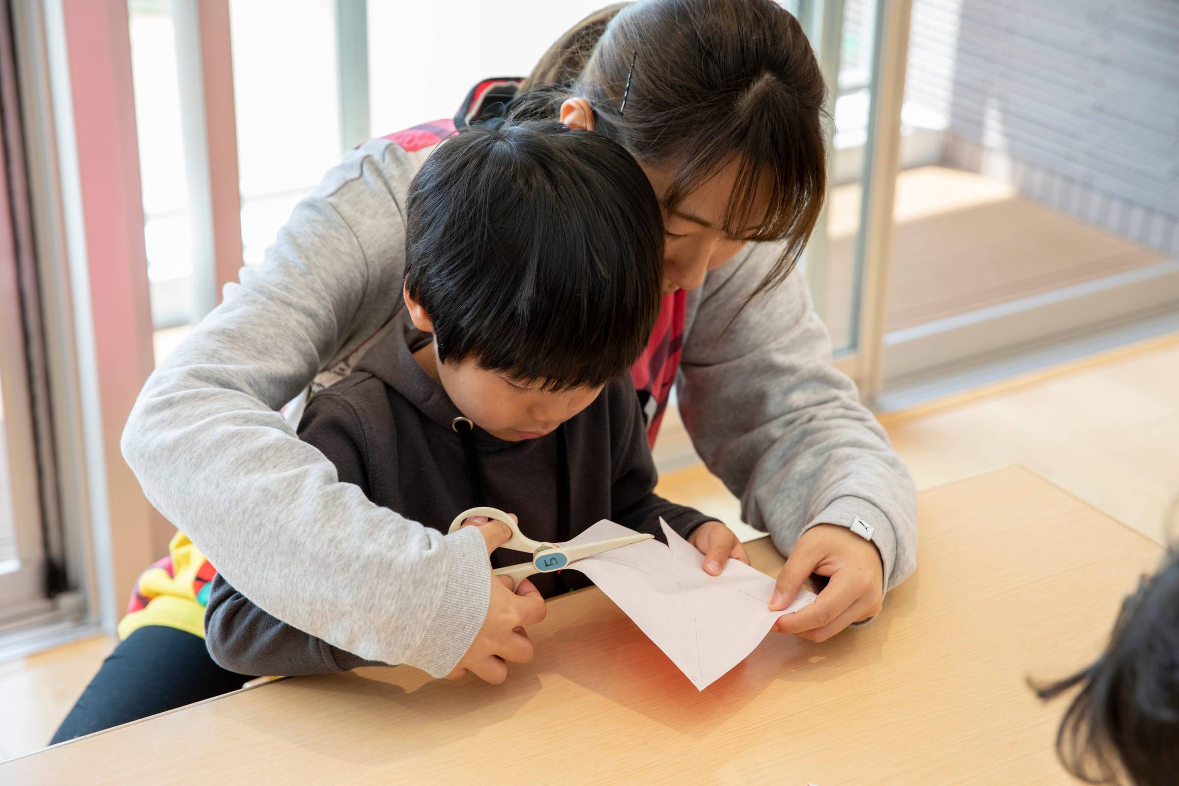 はさみで工作をする子どもを見守り、手を添える保育教諭