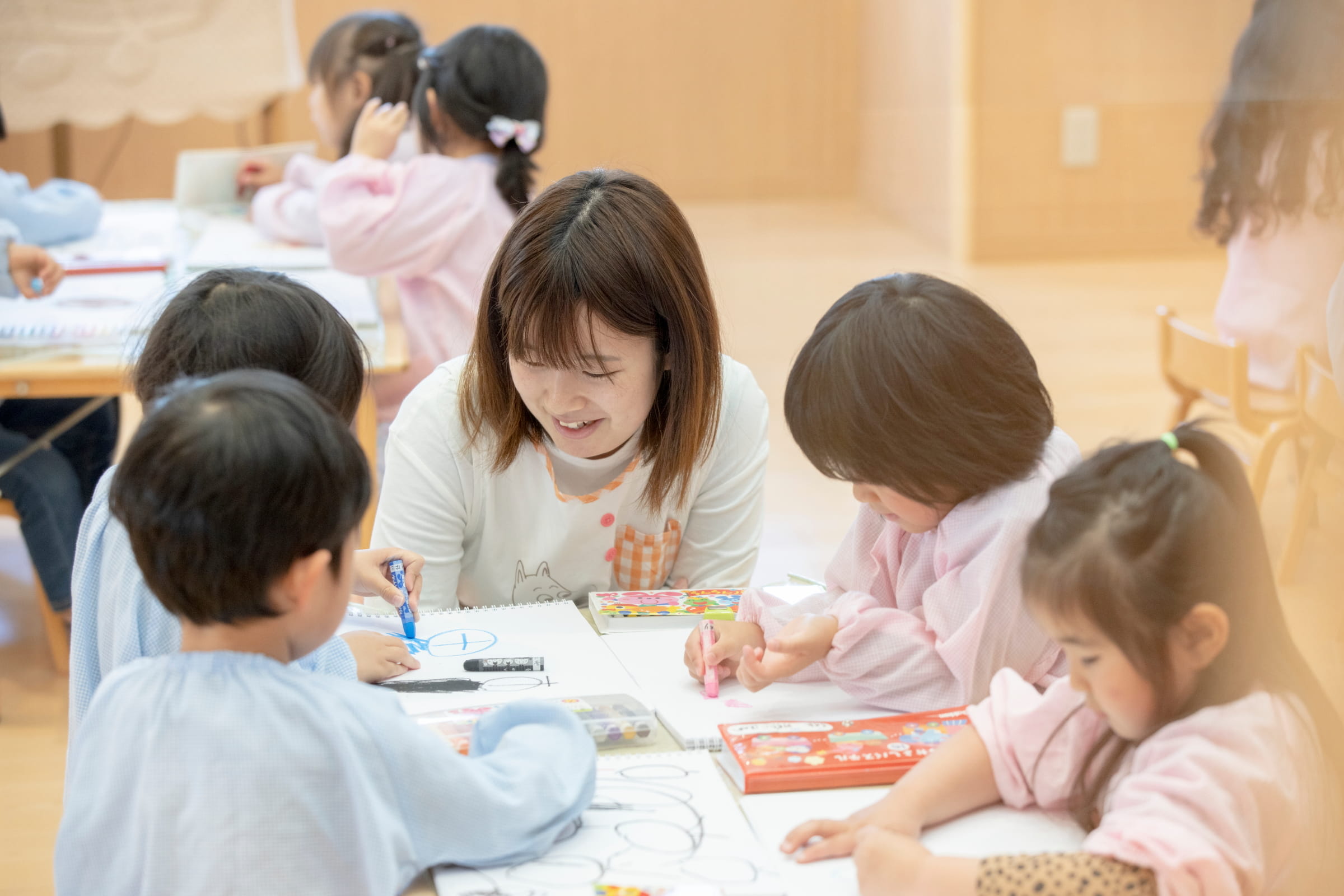 子どもたちと一緒に机に向かい制作活動をサポートするフリー・補助保育スタッフ